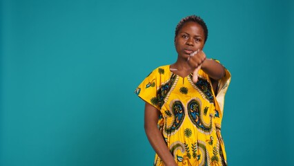 Dissatisfied person showing thumbs down symbol in studio, expressing her disapproval against blue...
