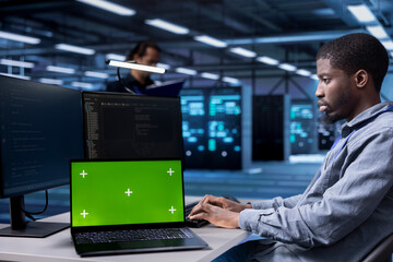 Engineer in data center running system diagnostic tests using isolated screen laptop. African american man in server farm deploying error checking utilities on mockup notebook to repair network issues