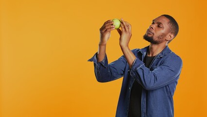 Male model examining a green apple to be clean after harvesting, guaranteeing the ripeness of locally grown fruits. Young adult supporting sustainable lifestyle concept. Camera B.