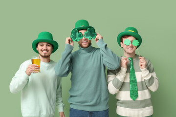 Happy young men in leprechaun's hats with beer, clovers and party glasses on green background. St....