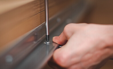 The hands of a caucasian young man twisting a screw with a screwdriver connecting a metal part to a wooden bed