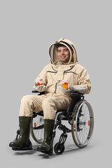 Male beekeeper in wheelchair with jars of honey on light background