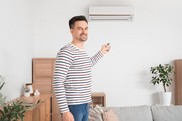 Handsome man turning on air conditioner at home