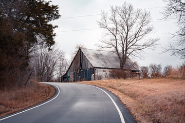 Rural scene with road leading to wooden abandoned barn 