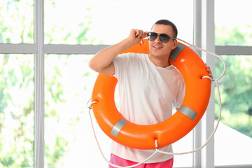 Happy male lifeguard with ring buoy and sunglasses near window in pool