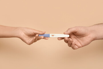 Hands of loving young couple with pregnancy test on beige background