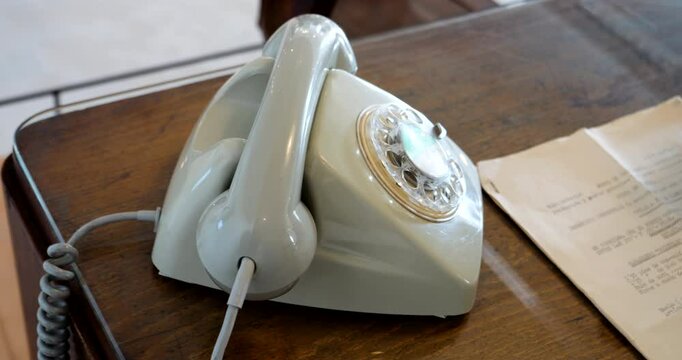A vintage colorful corded phone sits on a table in a room, positioned near an old printer with a document inside