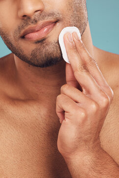 Hand, cotton pad and face with man, studio and skincare with hygiene, cleaning and grooming by blue background. Person, model and beard with dermatology, wellness and cosmetics for transformation