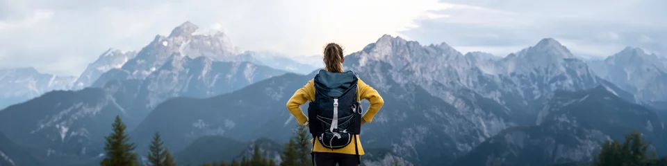 View from behind of a female hiker with backpack standing on top of a mountain looking at beautiful view © Gajus