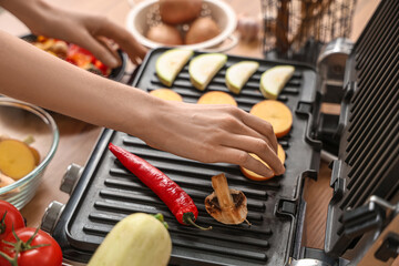 Young woman cooking tasty vegetables on modern electric grill in kitchen