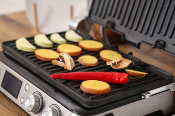 Modern electric grill with fresh vegetables on table in kitchen