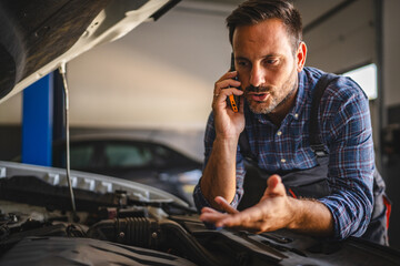 Car mechanic on mobile phone discuss car repair in garage workshop