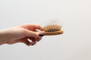A beautifully manicured hand holds a wooden comb filled with tangled fallen hair, avitaminosis,...