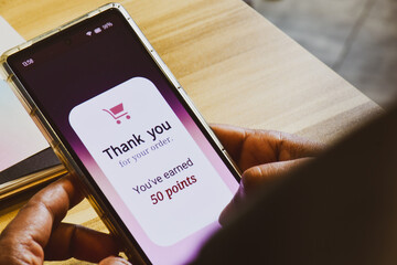 Smartphone screen showing a man earned 50 reward points by shopping online. E-commerce loyalty program concept, selective focus.