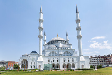 Grand white mosque with four minarets dominates skyline, arched entrance and domed roof gleam in sunlight.