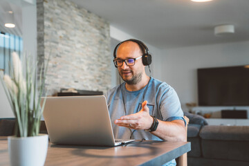 Caucasian man sitting in the dining room, wearing headphones - Conference call from home