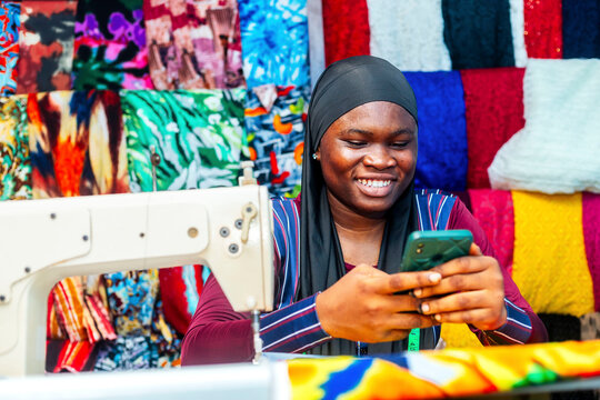 Happy female black seamstress using smartphone while isolated over a beautiful fabric background 