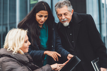 Group of three people of different age and ethnicity looking at a tablet oudoors
