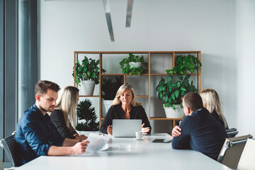 Senior woman CEO seating on the head of the table with her laptop in front of her leading the meeting