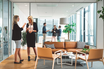 Two businesswomen having a discussion in a modern office with glass walls