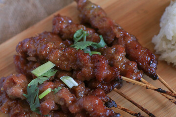 Grilled pork skewers or moo ping eat with Sticky rice on wooden cutting board. Popular Thai street food.