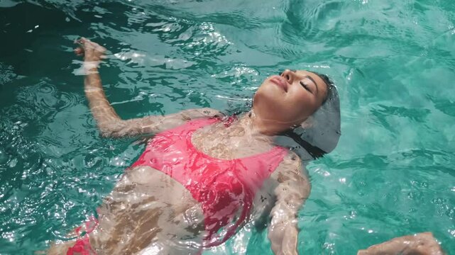 Beautiful girl in pink swimsuit floating in pool on her back. Relaxing in luxury pool
