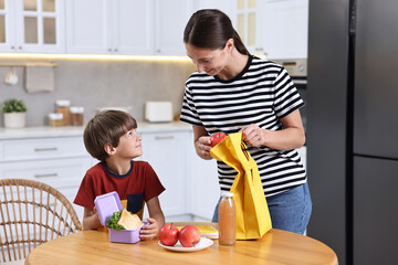 Fototapeta premium Mother and her cute son preparing lunch box with healthy food at wooden table in kitchen