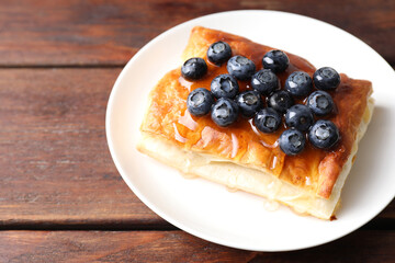 Tasty puff pastry with blueberries on wooden table, closeup