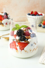 Tasty yogurt with fresh berries, granola and mint in glass on white table