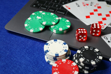 Poker chips, laptop, playing cards and dices on blue table. Online game