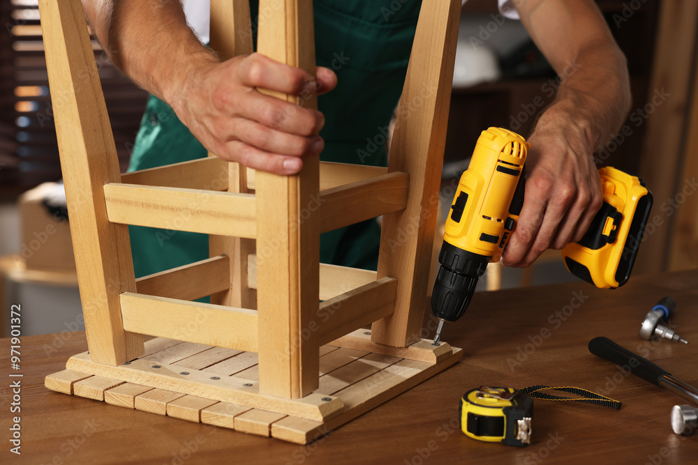 Sticker Man repairing wooden stool with electric screwdriver indoors, closeup