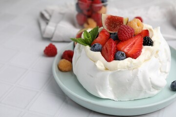 Pavlova cake (meringue dessert) with whipped cream, fresh berries, mint and fig on white tiled table, closeup