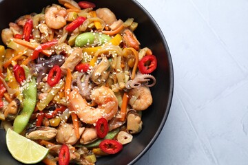 Stir-fry sea food in bowl on light grey table, top view. Space for text