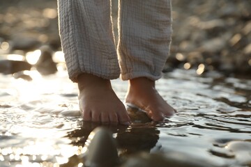 Cute little girl standing in water outdoors, closeup. Child enjoying beautiful nature