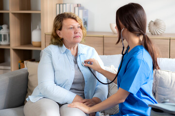 Obraz premium Caregiver young nurse woman examining elderly with stethoscope for checkup sitting on sofa in living room at home, nurse checkup patient about cardiac, patient and insurance, medical and health.