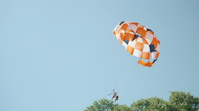 Two women are parasailing held by parachute tied to boat enjoying fun activity. Young female tourists having fun in water sport attraction next to the beach. Kiting over the sea during vacation