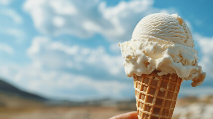 scoop of vanilla ice cream in waffle cone, against a summer blue sky