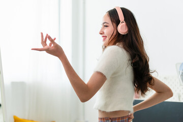 Portrait of young girl in headphones listening music and laughing while dancing in front of a mirror in bedroom