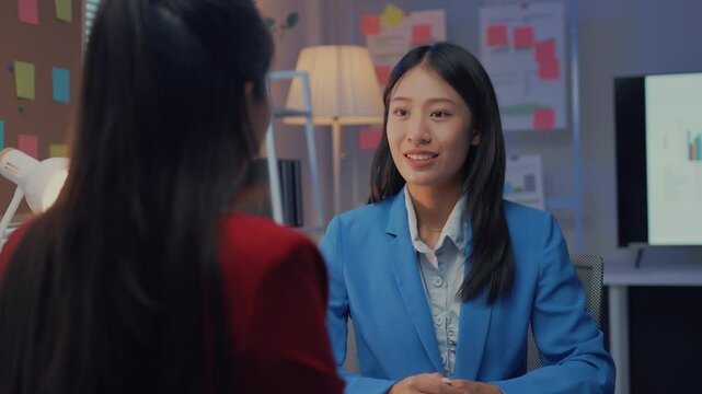 Young professional woman in a blue blazer is smiling during a job interview with a recruiter. The interview is taking place in an office setting