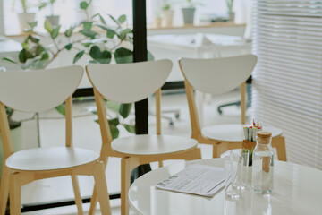 Bright and airy workspace featuring white chairs, a round table, and various green plants creating inviting and pleasant atmosphere for work and relaxation