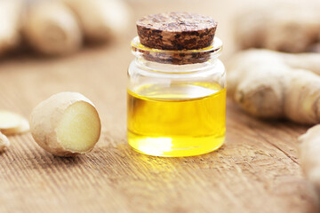 Ginger essential oil or extract in glass bottle with slices of root on wooden background, closeup, natural medicine and healthy hair and skin treatment concept