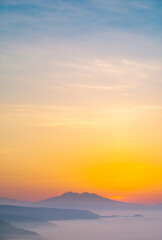 山の稜線のシルエット、オレンジ色と青のグラデーションの空。少し霞んだ印象の雄大な自然の風景美。