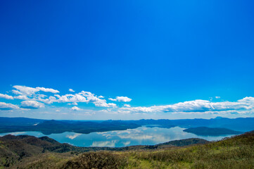 雲の浮かぶ青空を反射する湖と周囲の山々を見下ろす。爽快で清々しい晴れやかな自然の景色。