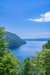 爽やかな青空の緑の木々との山間の湖の風景。北海道の摩周湖。