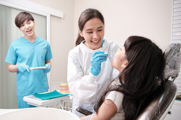 Fototapeta premium Asian female pediatric dentist and assistant check and examination a little girl's caries teeth in dental clinic, well-being hygiene, and professional orthodontic healthcare work in kid hospital.