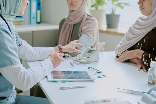 Healthcare professional speaking with veiled patient about medical results while using stethoscope and blood pressure monitor during consultation in office setting
