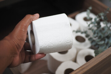 A Hand Grasping a Roll of Toilet Paper Stored Inside a Rustic Wooden Storage Box