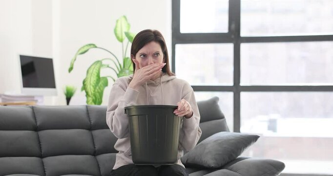 Woman looks worried as she sits on sofa with bucket