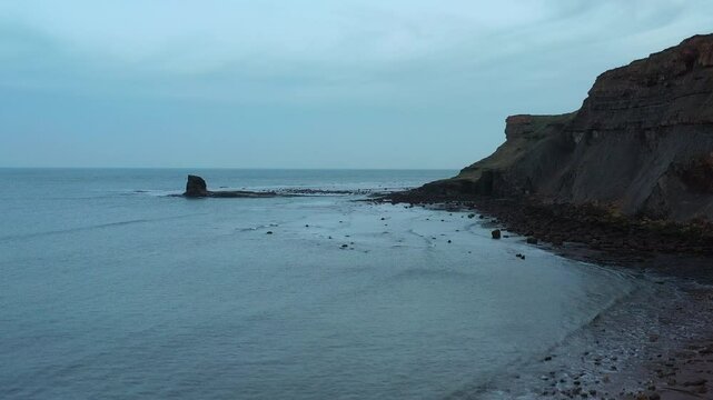 Aerial footage rising up from head height to look at the black nab at saltwick bay, yorkshire