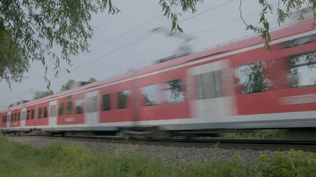 Red train speeds through green countryside on a cloudy day, motion blur, side view